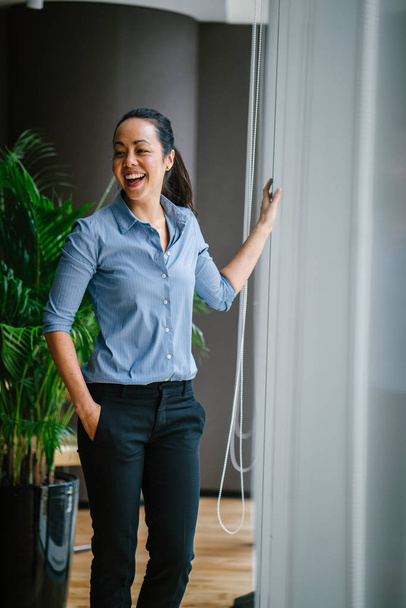 Portrait of young confident asian businesswoman laughing standing near window - Photo, Image