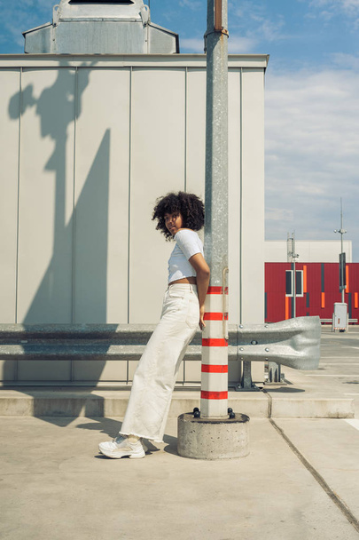 vista laterale di bella elegante giovane donna africana americana appoggiata al palo sulla strada
 - Foto, immagini
