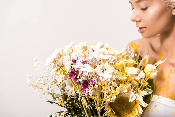 attractive woman with bouquet of flowers and yellow paint on body isolated on white - Photo, Image