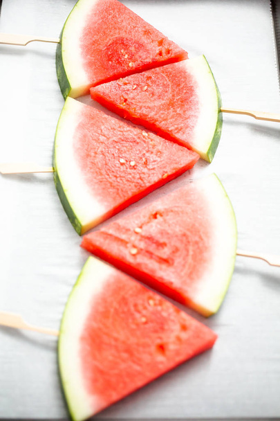 Sliced watermelon in triangle shapes on wooden sticks. - Fotó, kép