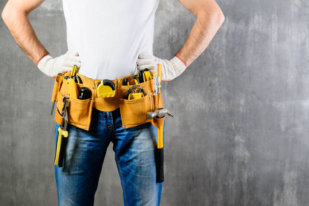 unknown handyman with hands on waist and tool belt with construc - Zdjęcie, obraz
