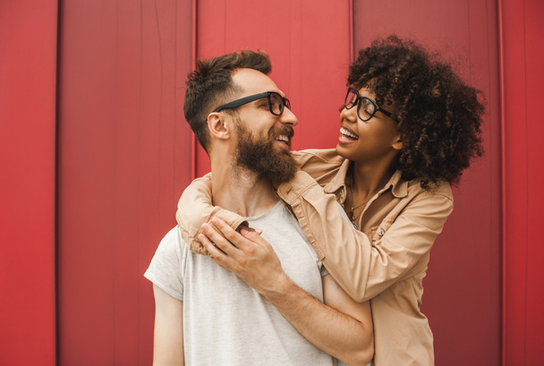 glückliches junges interrassisches Paar mit Brille, das einander umarmt und lächelt - Foto, Bild