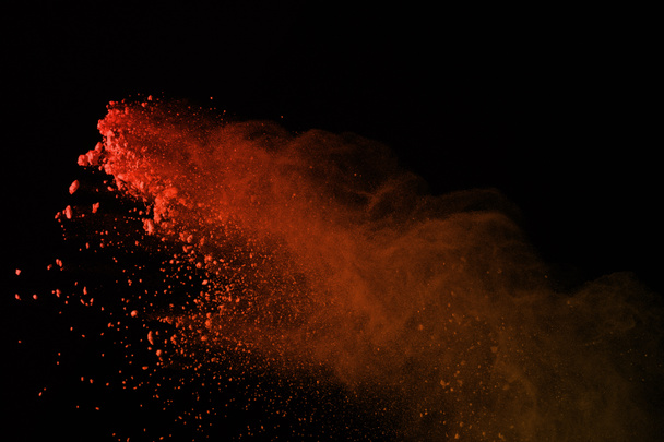 Gefrierbewegung von bunten Pulverexplosionen isoliert auf schwarzem Hintergrund. roter Staub explodiert auf dunklem Hintergrund. - Foto, Bild