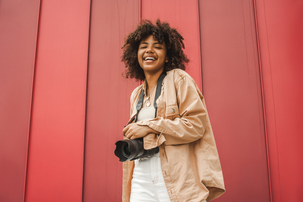 niski kąt widzenia wesoły młodych african american kobieta trzymając aparat i uśmiecha się do kamery - Zdjęcie, obraz