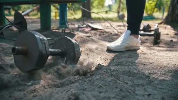 Zware ijzeren halter valt op het zand voor de voeten van atleet in witte sneakers - Video