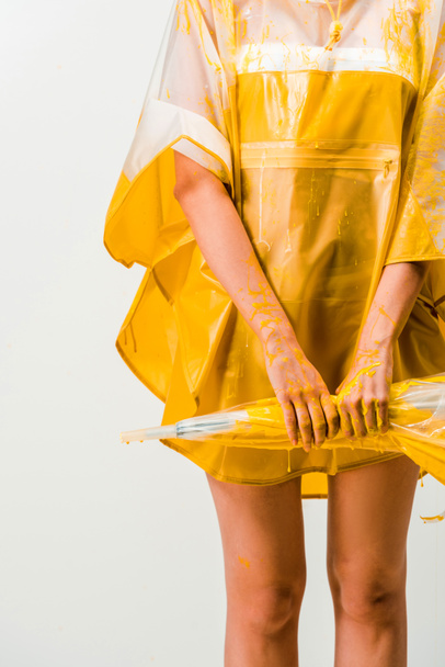 cropped image of woman in raincoat painted with yellow paint holding umbrella isolated on white  - Foto, immagini