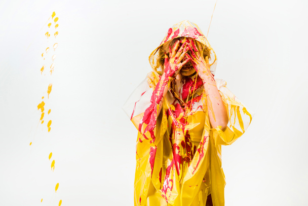 woman in raincoat painted with yellow and red paints protecting face from paints isolated on white - 写真・画像