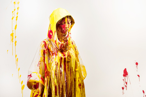 beautiful woman in raincoat painted with yellow and red paints standing with closed eyes isolated on white - Foto, Bild