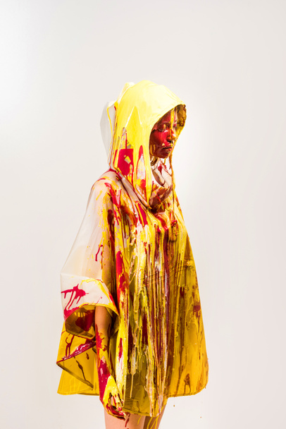 beautiful woman in raincoat painted with yellow and red paints standing in hood isolated on white - Foto, afbeelding