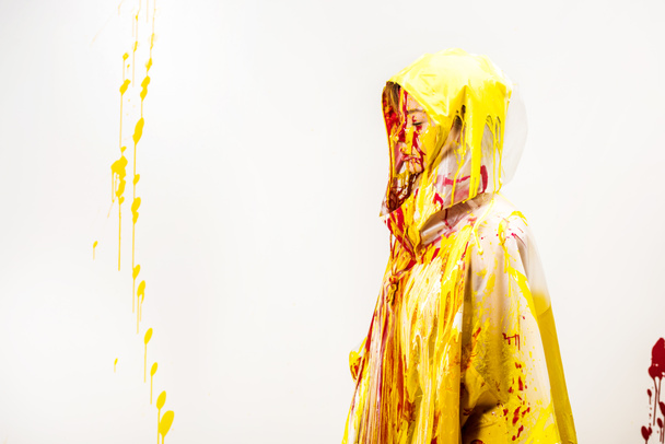 side view of woman in raincoat painted with yellow and red paints standing in hood isolated on white - Foto, afbeelding