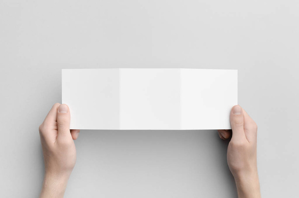 Square Tri-Fold Brochure Mock-Up - Male hands holding a blank tri-fold on a gray background. - Foto, Imagen