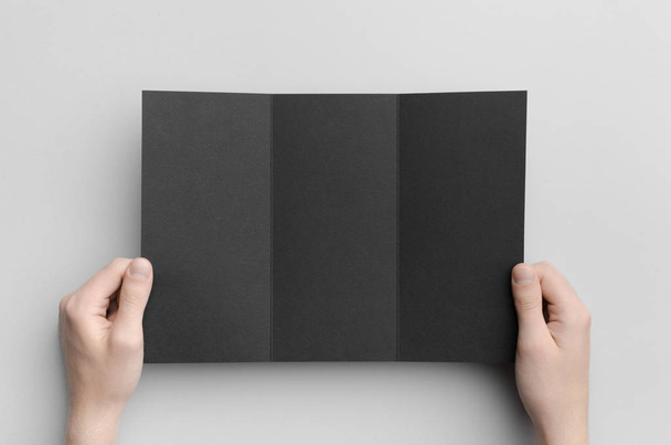 Black A4 Tri-Fold Brochure Mock-Up - Male hands holding a black tri-fold on a gray background. - Foto, Bild