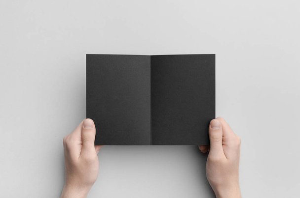 Zwarte A6 Bi-Fold / tweeën gevouwen Brochure Mock-Up - mannelijke handen houden een zwarte bi-fold op een grijze achtergrond. - Foto, afbeelding