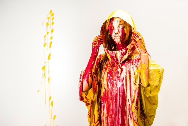 beautiful woman in raincoat painted with yellow and red paints wearing hood isolated on white - Fotoğraf, Görsel