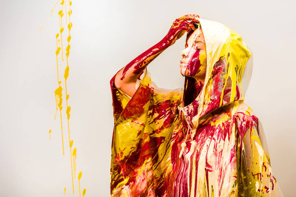 side view of woman in raincoat painted with yellow and red paints taking off hood isolated on white - Foto, imagen