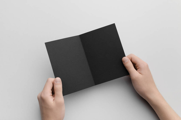 Black A6 Bi-Fold / Half-Fold Brochure Mock-Up - Male hands holding a black bi-fold on a gray background. - 写真・画像
