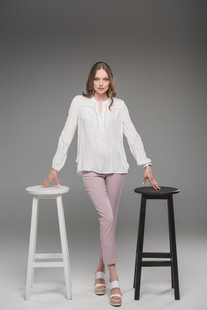 elegant woman posing between two chairs on grey background  - Photo, Image
