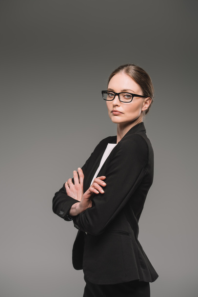 confident businesswoman in eyeglasses standing with crossed arms isolated on grey background  - Photo, Image