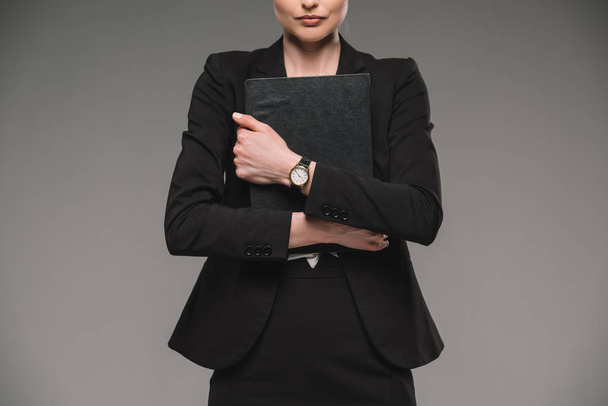 abgeschnittenes Bild einer Geschäftsfrau mit Lehrbuch auf grauem Hintergrund  - Foto, Bild