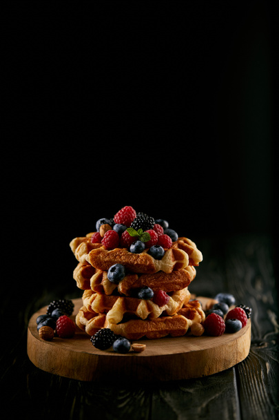 tasty stacked belgian waffles with berries on wooden cutting board on black - Foto, imagen