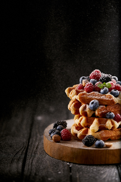 tasty belgian waffles with sugar powder spilling from side on black - Foto, afbeelding