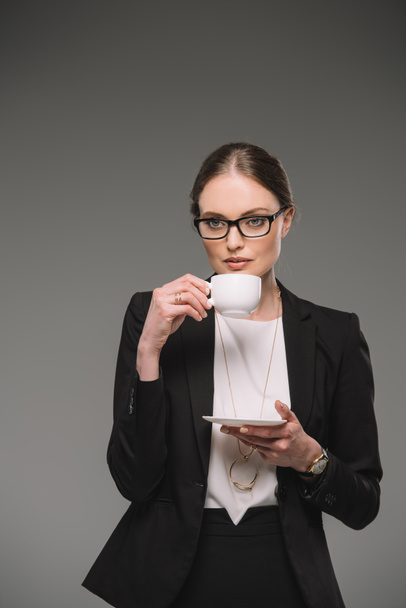 atrakcyjna kobieta interesu w okularach picia kawy z kubek na białym tle na szarym tle  - Zdjęcie, obraz