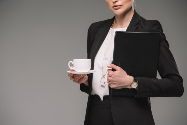 cropped image of businesswoman holding cup of coffee and textbook isolated on grey background  - Foto, afbeelding