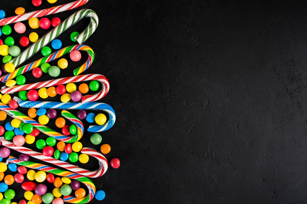 Christmas candy cane with candy drops over black background with copy space, flat lay - Fotoğraf, Görsel