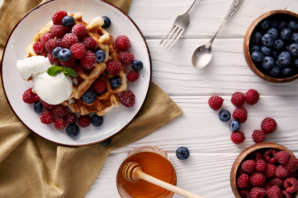freshly baked belgian waffles with honey, ice cream and berries on white wooden table - Foto, Bild