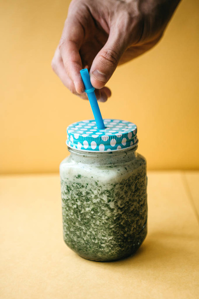 Vegetarian green mix of vegetable and fruit cocktail from cucumber and green parsley and dill. The person takes a jar with a hand to drink - 写真・画像