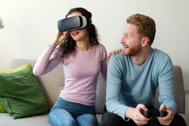 Happy young couple playing video games with virtual reality headsets at home - Fotoğraf, Görsel