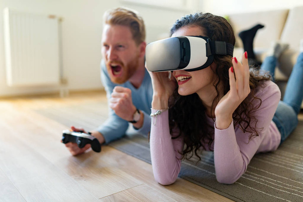 Happy young couple playing video games with virtual reality headsets at home - Photo, image