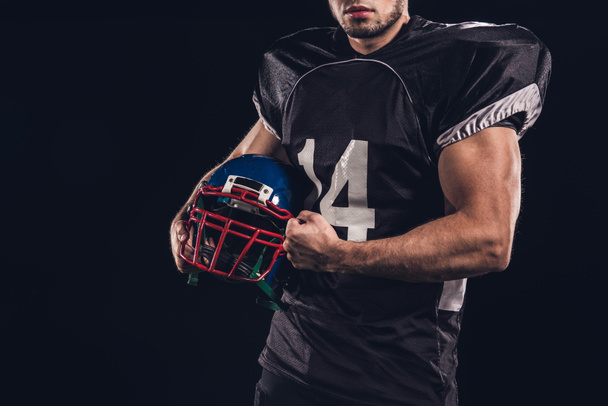 cropped shot of muscular american football player holding helmet isolated on black - Photo, Image