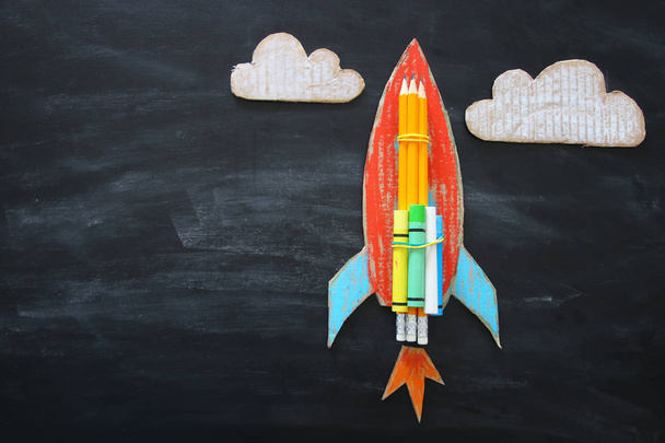 Back to school concept. Top view image of handmade cardboard rocket and clouds with pencils over classroom blackboard background. - Fotografie, Obrázek
