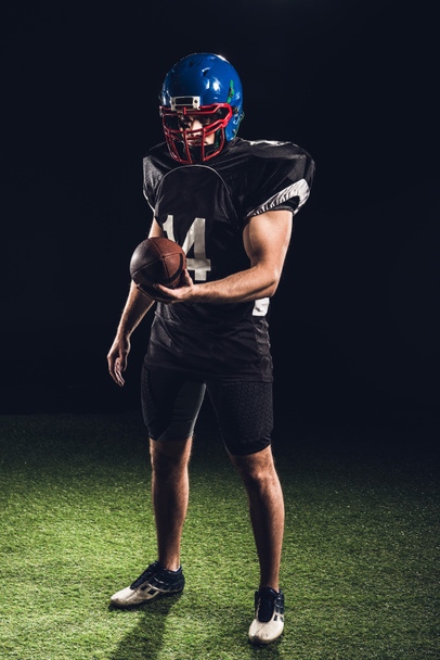 handsome american football player with ball looking at camera on black - Foto, immagini