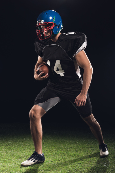 american football player with ball on green grass on black - Φωτογραφία, εικόνα