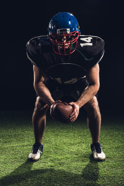 joueur de football américain debout sur l'herbe avec balle et regardant la caméra sur noir
 - Photo, image