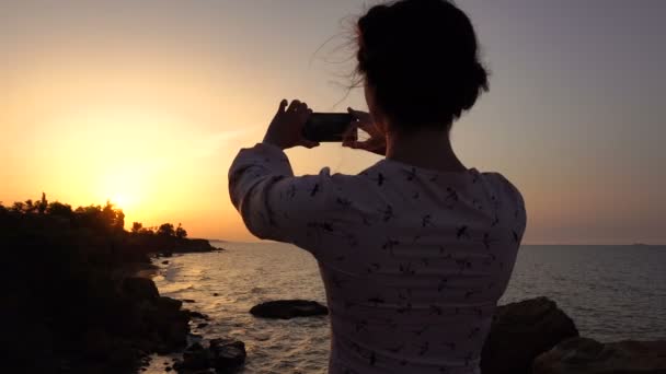 Rozkošný kavkazské bruneta dívka v lehké šaty pomocí Smartphone záběr na útesu nad mořem v době východu slunce - Záběry, video