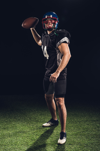 american football player on green grass throwing ball on black - Photo, Image