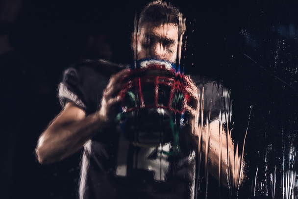 weergave van Amerikaans football-speler vasthouden helm zwart door natte glas - Foto, afbeelding