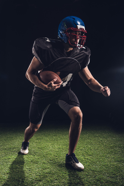 american football player holding ball and running on field on black - 写真・画像