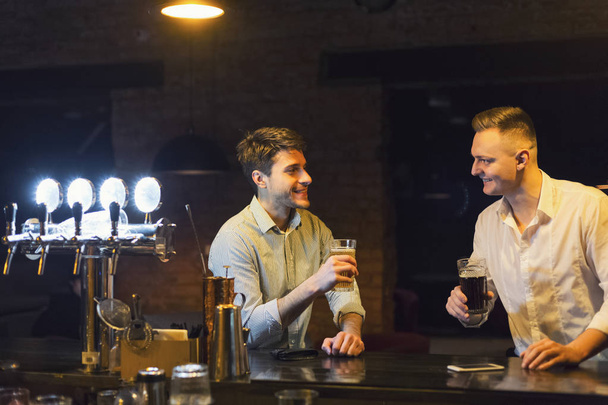 Deux jeunes hommes heureux parlent et boivent de la bière au bar
 - Photo, image