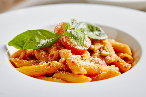 Tomato Penne Pasta Al Dente with Tomato Sauce, Parmigiano Reggiano Cheese, Cherry Tomatoes and Basil in White Plate Close Up. Traditional Italian Macaroni in Restaurant - Foto, imagen