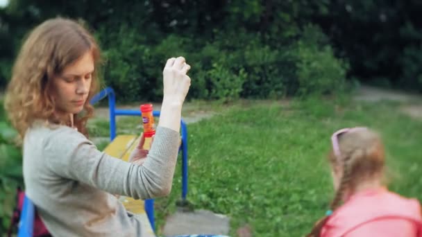 Happy Mother and her little Daughter playing together outdoor, blowing soap bubbles, having fun on backyard. Nature. Beauty Mum and her Child in Park together. Mom and Baby 4k - Video, Çekim