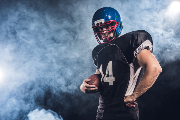 serious american football player with ball against white smoke - Foto, imagen