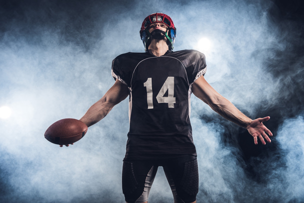 american football player with ball looking up against white smoke - Photo, Image