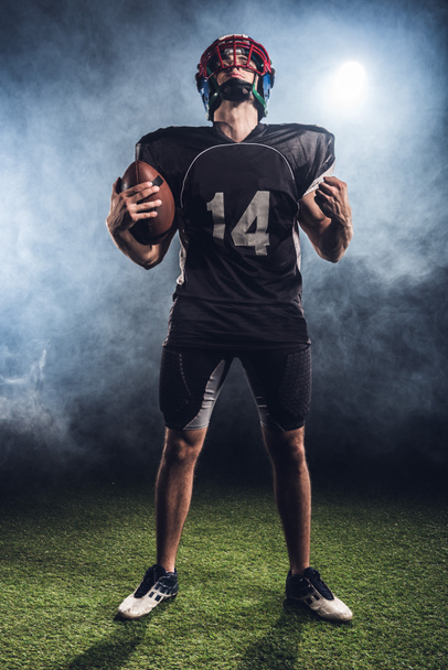 american football player with ball making fist and looking up against white smoke - Φωτογραφία, εικόνα