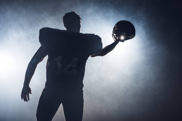 silhouet van american football speler holding helm tegen witte rook - Foto, afbeelding