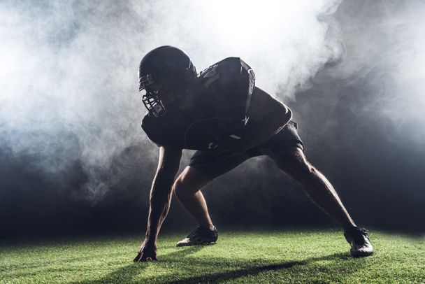silueta del jugador de fútbol americano en posición estelar contra el humo blanco
 - Foto, Imagen