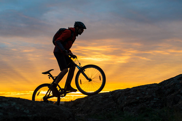 Cyclist in Red Riding the Bike on the Autumn Rocky Trail at Sunset. Extreme Sport and Enduro Biking Concept. - 写真・画像